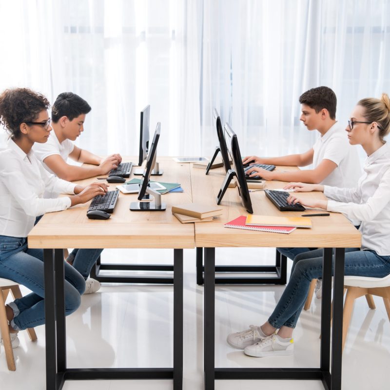 side view of four young multicultural students studying on computers